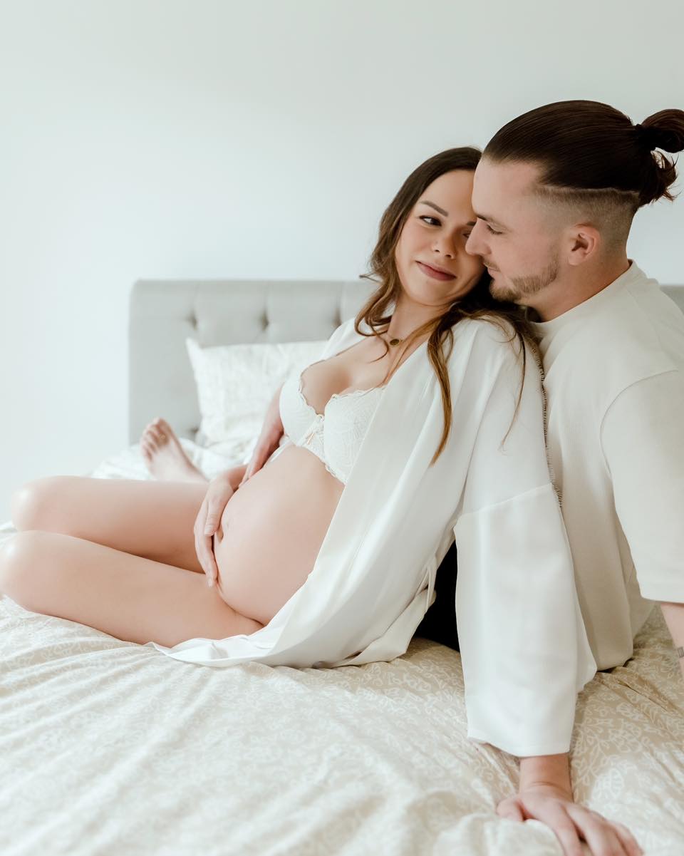 Couple attendant un bébé lors d'une séance photo grossesse en studio à Annemasse. L'homme entoure tendrement la femme enceinte vêtue de blanc.
