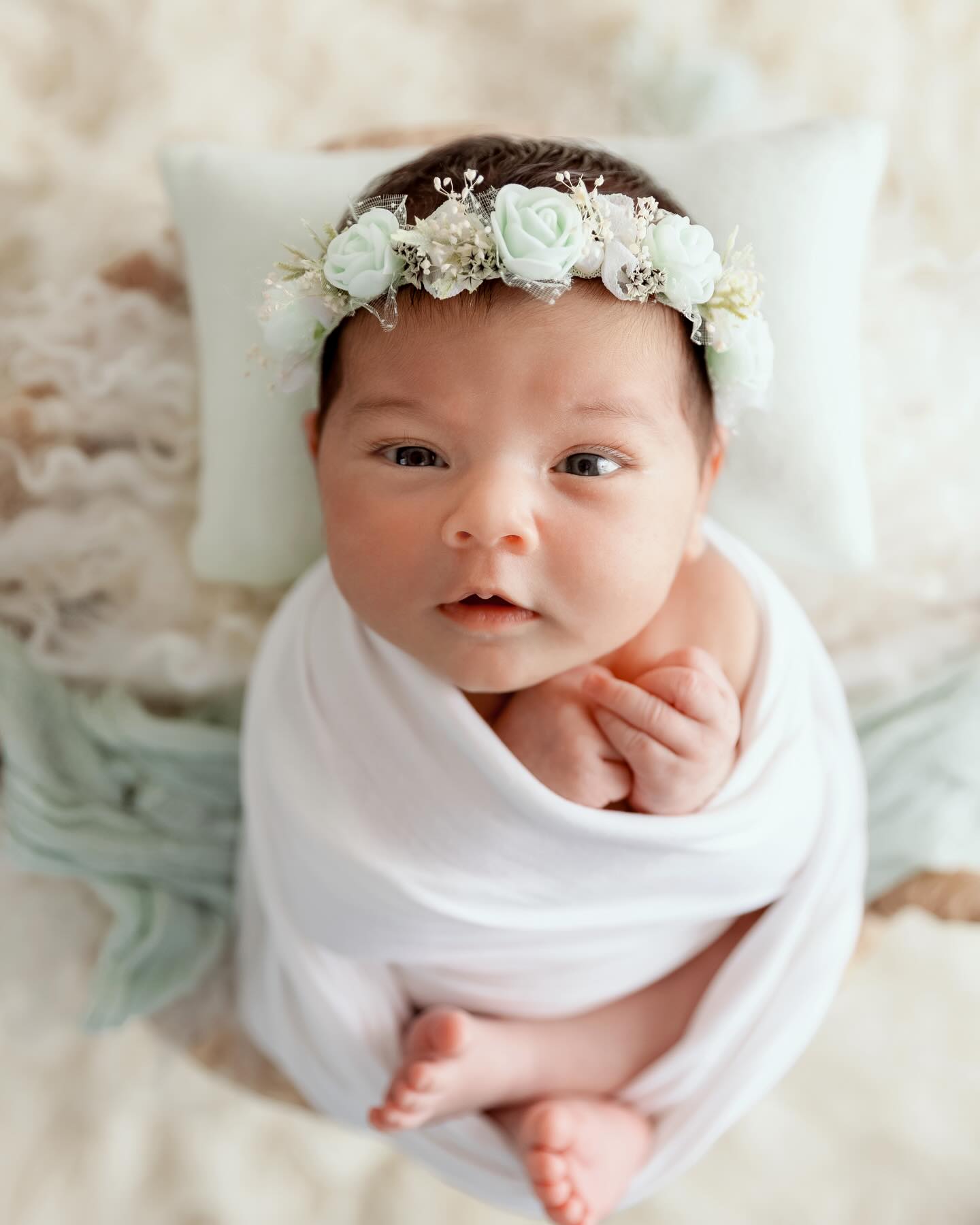 Bébé nouveau-né enveloppé de blanc avec couronne de fleurs blanches en studio photo