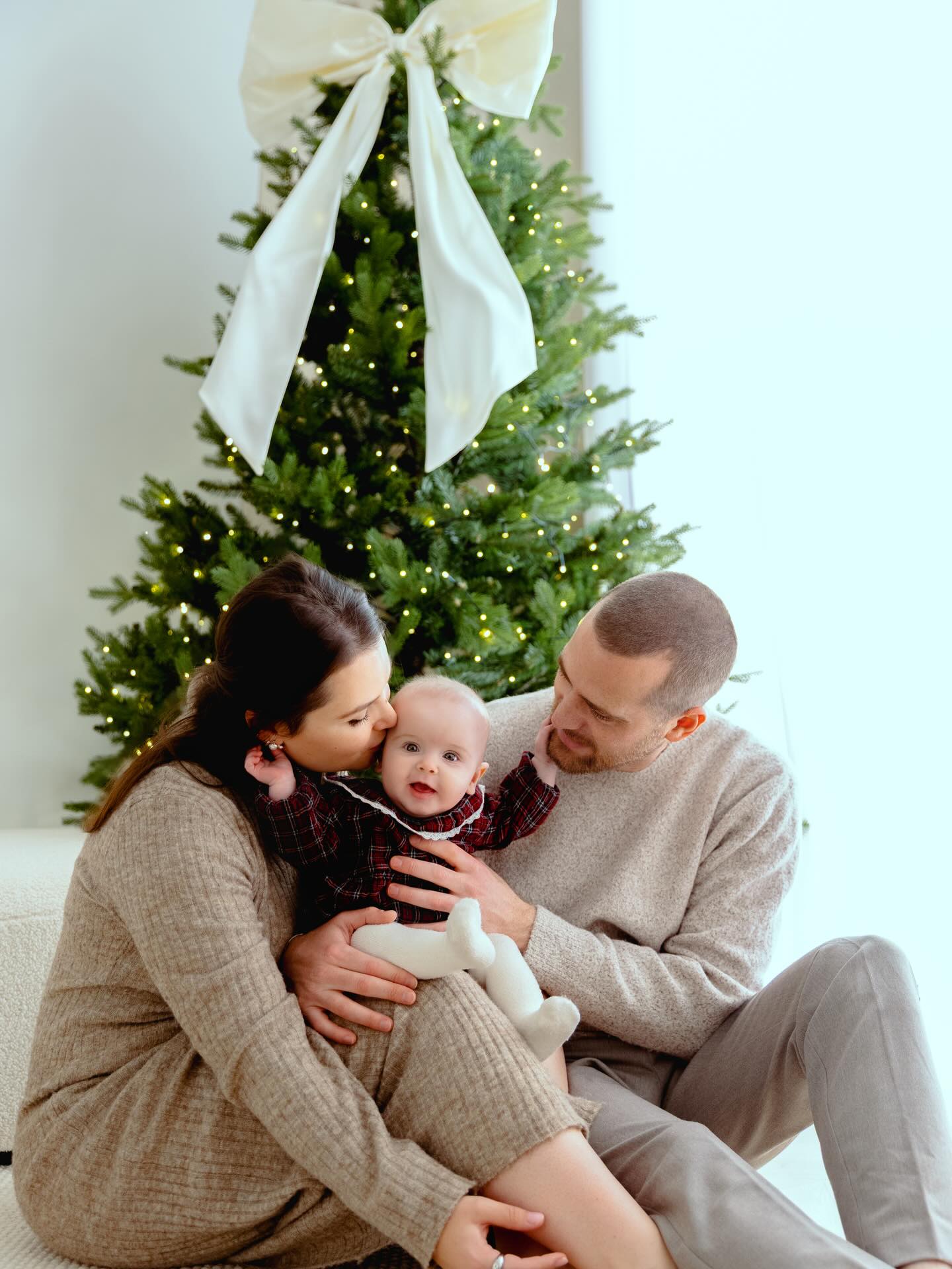 Famille avec bébé posant devant sapin de Noël illuminé avec ruban blanc, studio photo Haute-Savoie