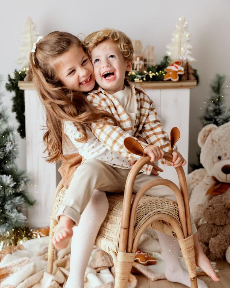 Deux enfants souriants lors d'une séance photo de famille festive en studio en Haute-Savoie, avec décoration de Noël et traîneau en bois