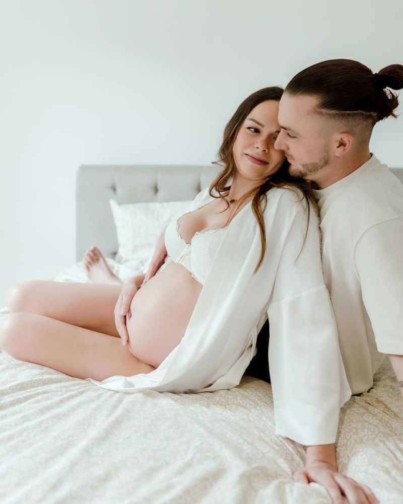 Couple attendant un bébé lors d'une séance photo grossesse en studio à Annemasse. L'homme entoure tendrement la femme enceinte vêtue de blanc.