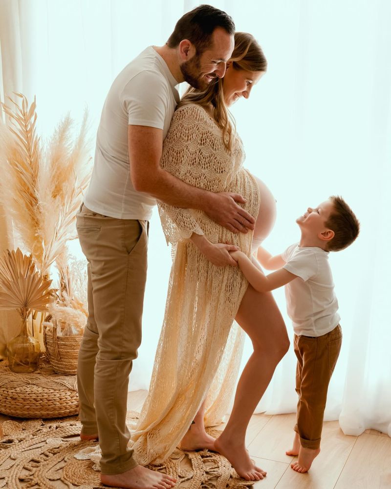 Famille heureuse avec femme enceinte, père et enfant en tenue beige, décoration bohème naturelle, photographe famille en Haute-Savoie