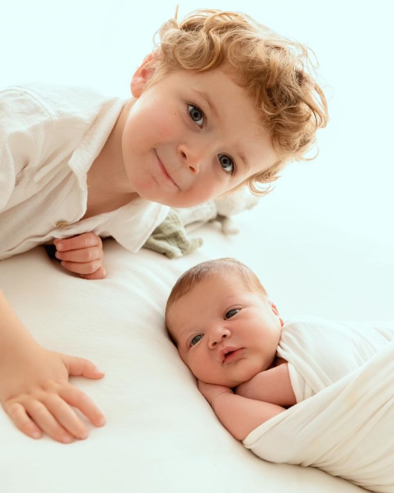 Grand frère et bébé nouveau-né en tenue blanche, photo de famille tendresse à Annemasse