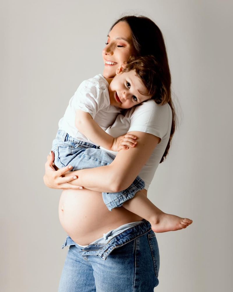 Femme enceinte souriante tenant son enfant en studio, photo de maternité professionnelle près de Genève
