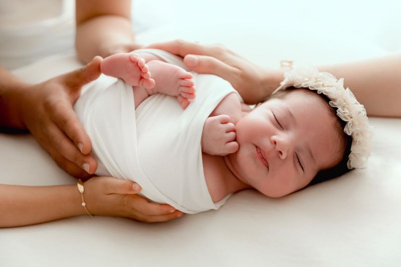 Nouveau-né endormi avec bandeau dentelle, mains des parents, photographie studio douce et émotionnelle, photographe nouveau-né entre Genève et Annecy