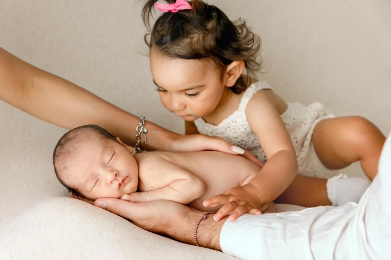 Grande sœur découvrant tendrement son petit frère nouveau-né lors d'une séance photo famille en studio, photographe famille à Annemasse, près de Genève