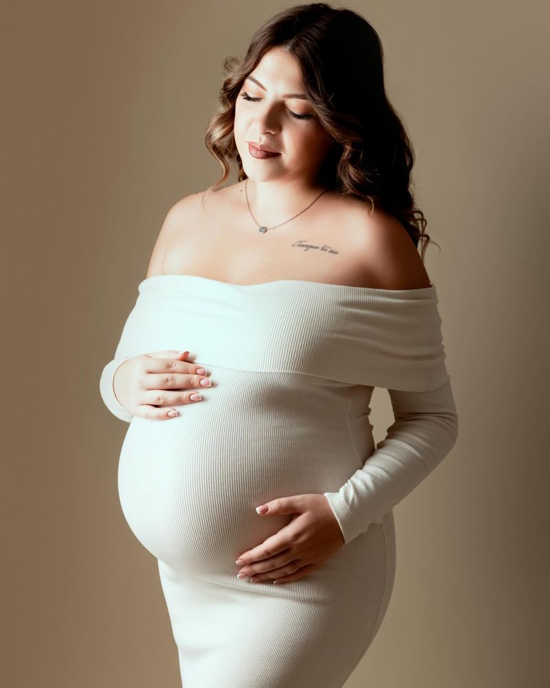Femme enceinte en robe blanche posant délicatement en studio photo. Séance maternité professionnelle en Haute-Savoie.