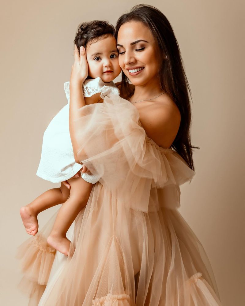 Mère tenant sa fille dans ses bras, vêtues de robes tulle beige clair, sourire complice, fond neutre studio, photographe famille entre Genève et Annecy