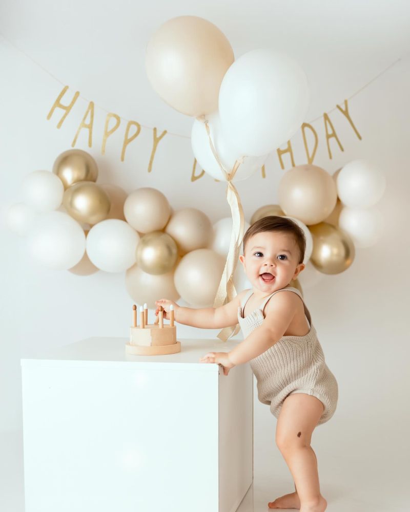 Bébé souriante tenant un ballon lors d'une séance photo d'anniversaire 1 an en studio, décoration ballons blanc et, photographe bébé à Annemasse, près de Genève