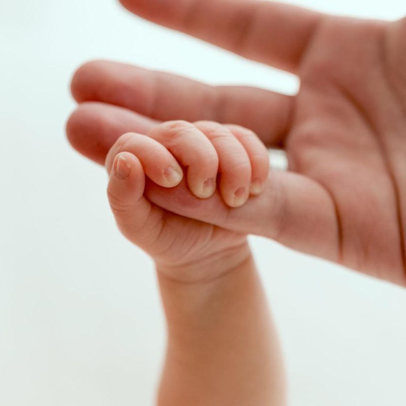 Tiny hand of newborn baby holding parent's finger, tender moment captured by newborn photographer in Annemasse