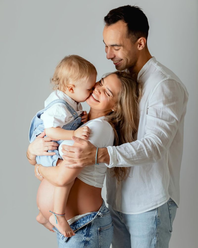 Famille heureuse avec jeune enfant lors d'une séance photo studio. Parents et bébé posent ensemble sur fond neutre gris., photographe famille à Annemasse