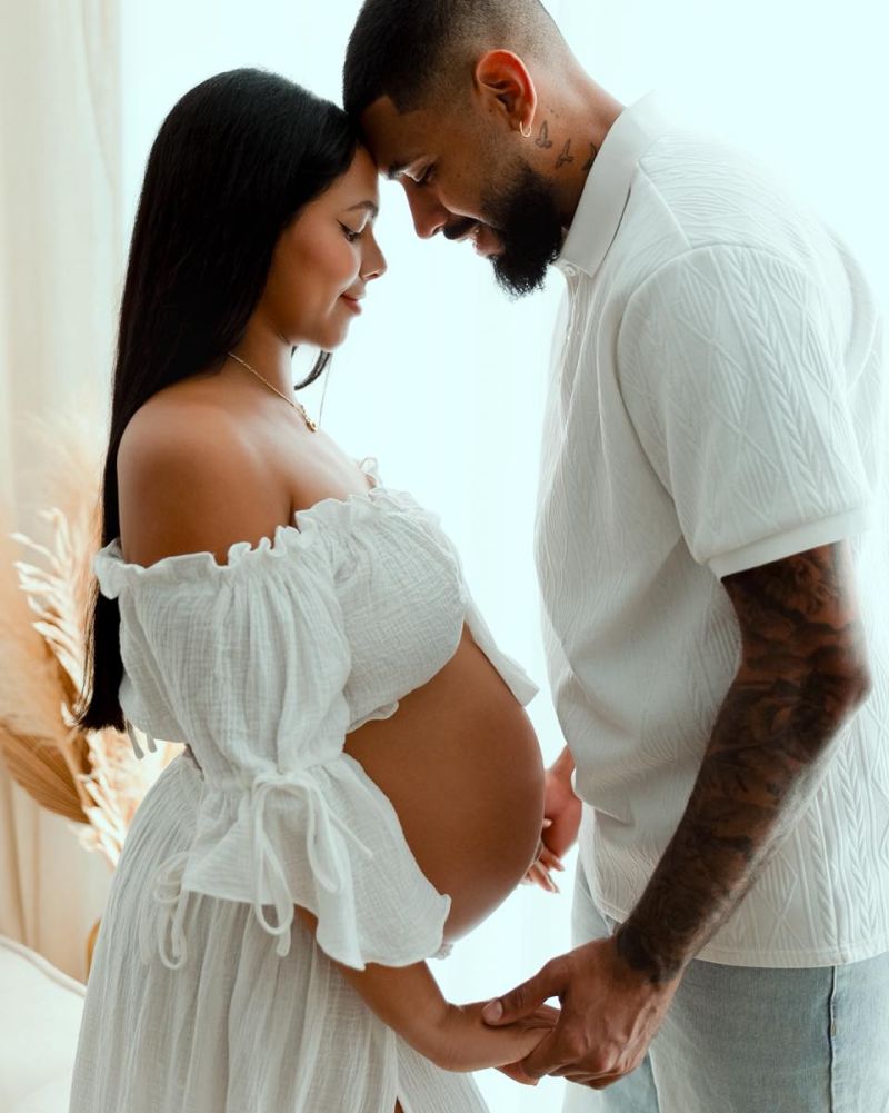 Couple attendant un enfant lors d'une séance photo grossesse en studio près de Genève. Femme enceinte vêtue d'une robe blanche, homme embrassant le ventre.
