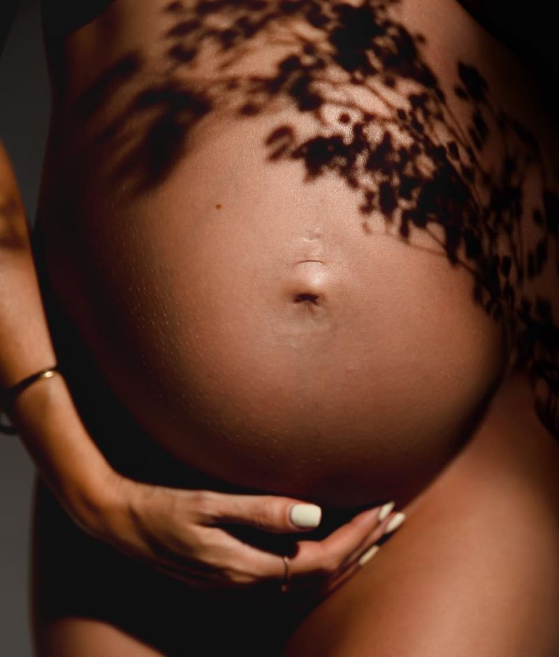 Femme enceinte avec jeu de lumière créant des ombres délicates sur son ventre arrondi, photographe grossesse à Annemasse