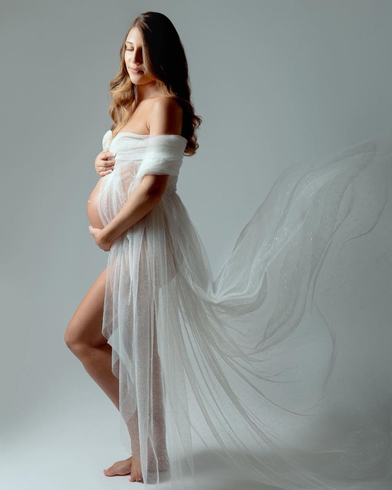 Femme enceinte en robe blanche vaporeuse posant en studio avec voile fluide, photographe grossesse près de Genève
