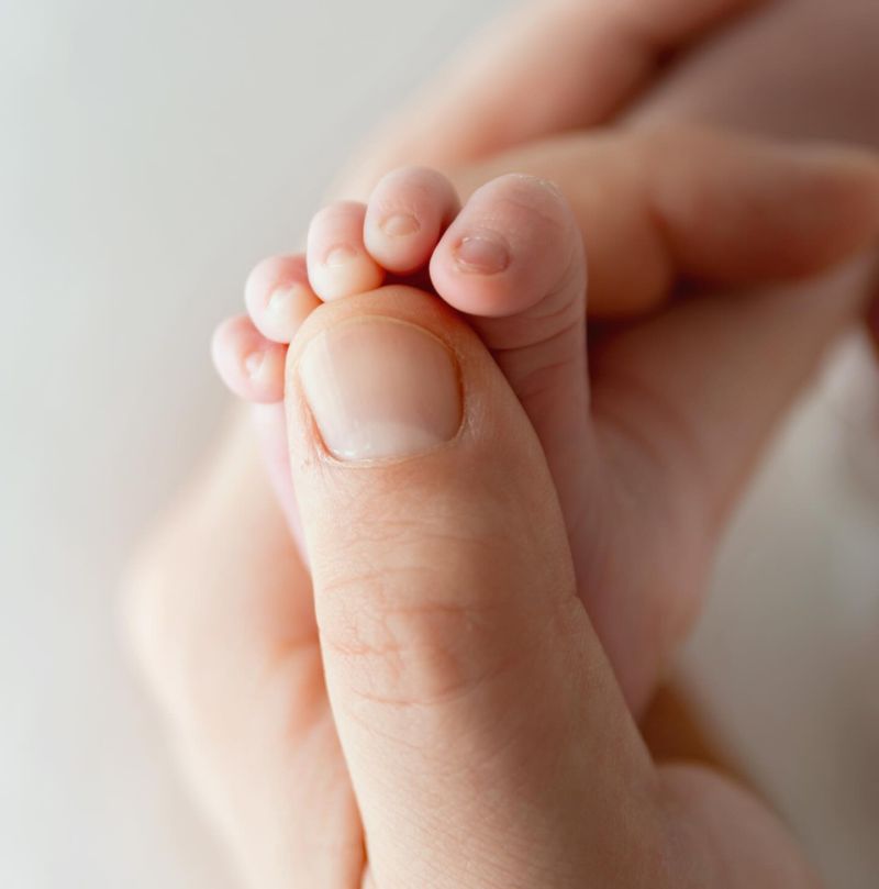 Gros plan délicat des petits pieds d'un nouveau-né tenant le doigt d'un adulte, photographe spécialisée nouveau-né Annemasse