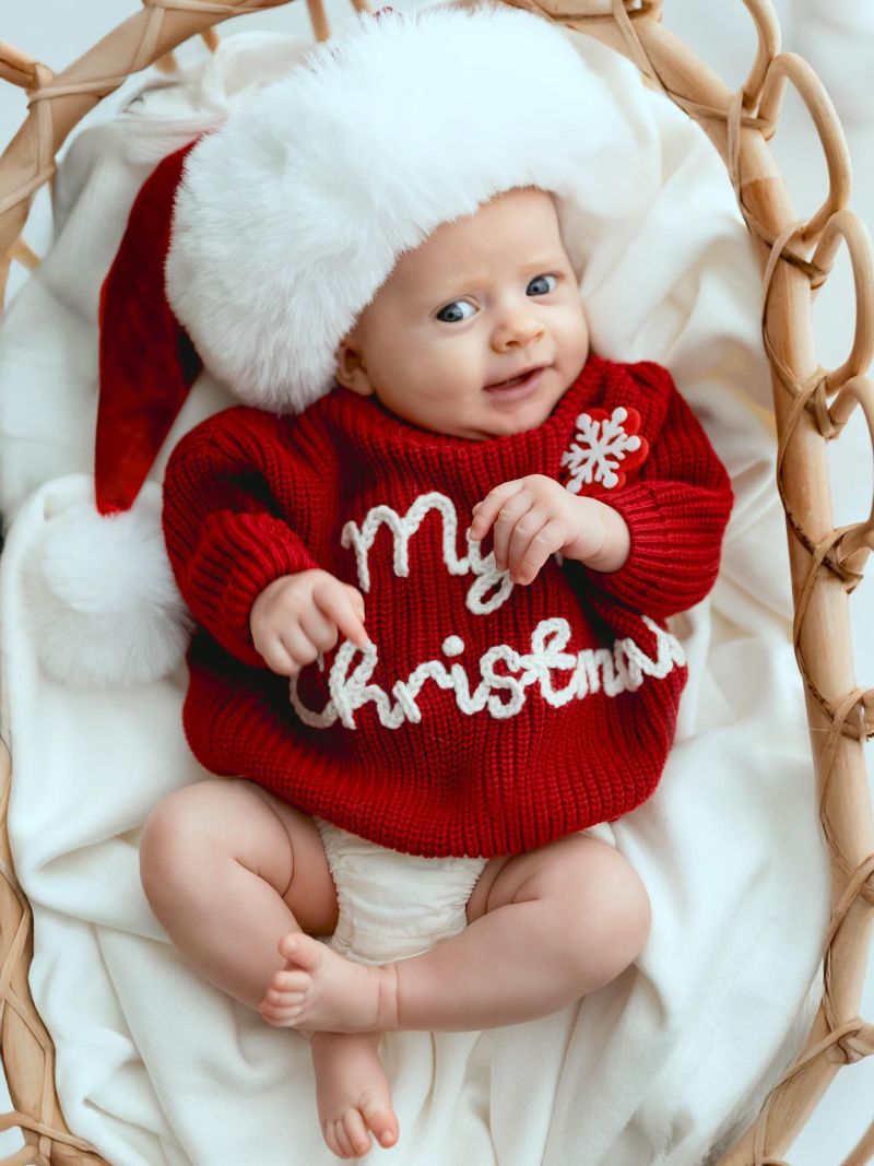 Bébé souriant en tenue de Noël rouge et bonnet blanc, photo studio professionnelle entre Genève et Annecy