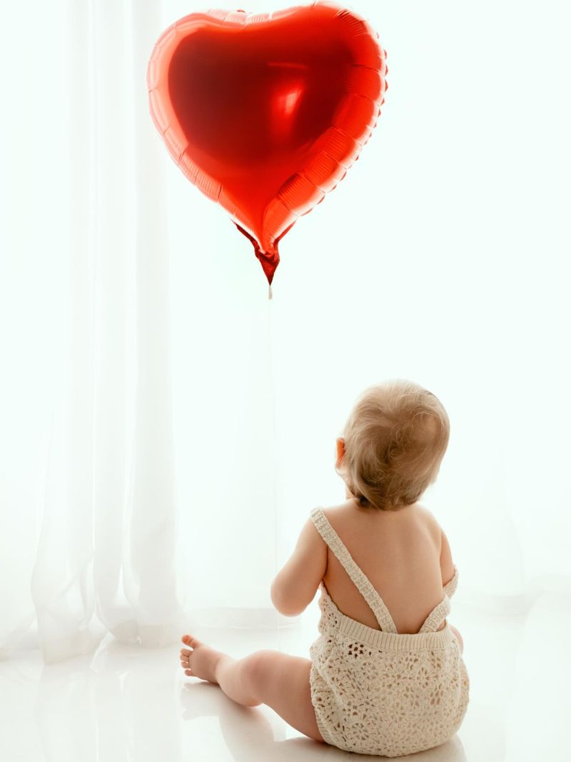 Bébé de dos regardant un ballon cœur rouge, séance photo studio professionnelle à Annemasse