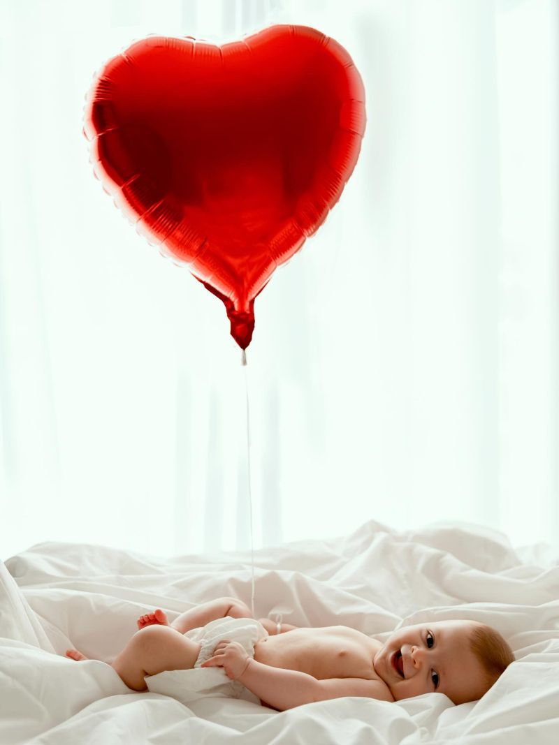 Bébé souriant sous un ballon cœur rouge, séance photo nouveau-né en studio entre Genève et Annecy
