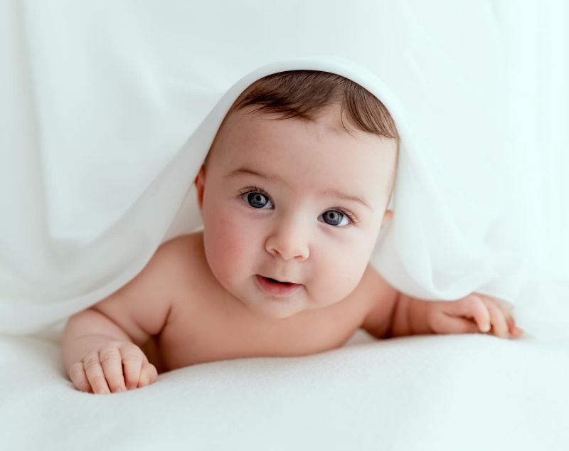 Bébé souriant enveloppé de blanc, photographe bébé spécialisée près de Genève