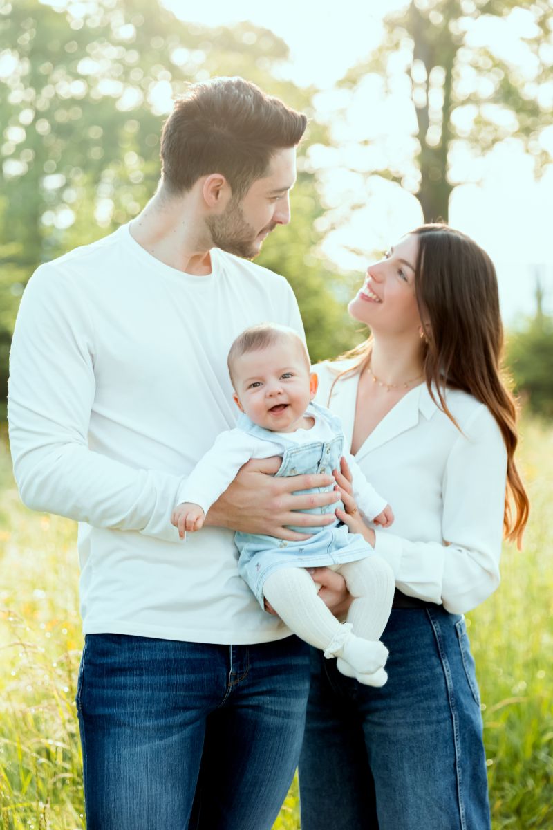 Portrait de famille souriant avec bébé dans un parc ensoleillé. Photographe bébé près de Genève