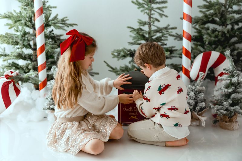 Deux enfants souriants en tenue de Noël dans un décor festif avec cannes de bonbon et sapin enneigé. Photographe bébé en Haute-Savoie
