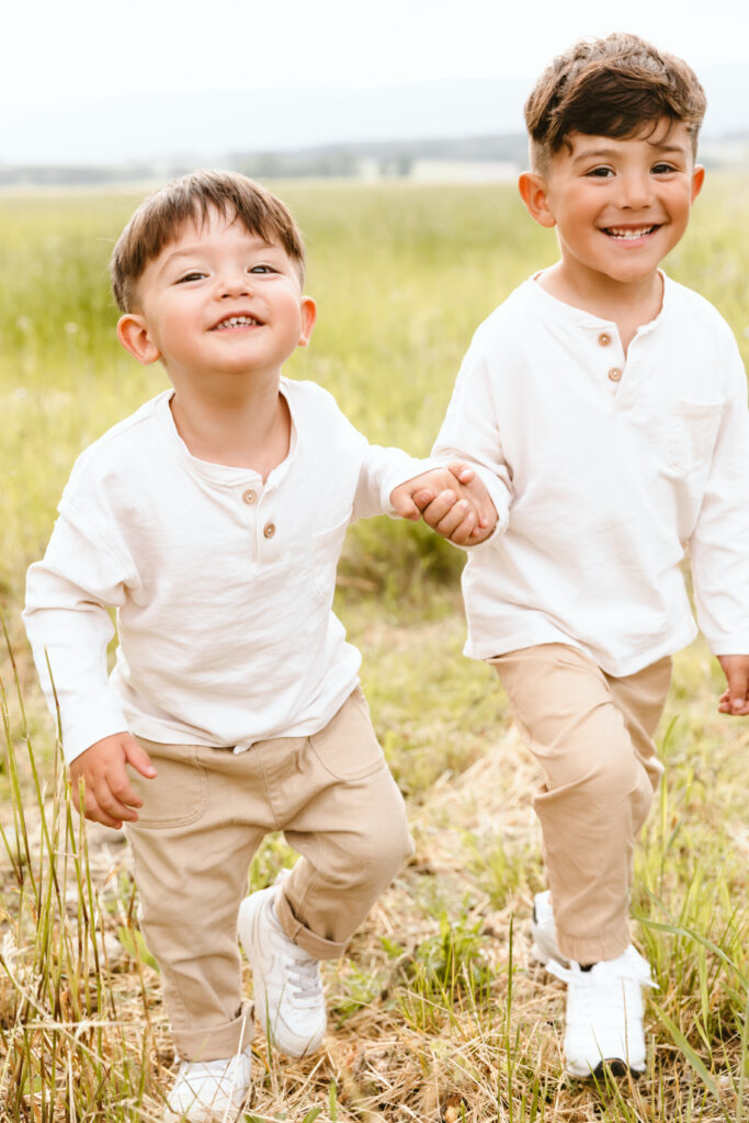 Two young boys smiling and holding hands in a field, family photographer in Annemasse, Haute-Savoie