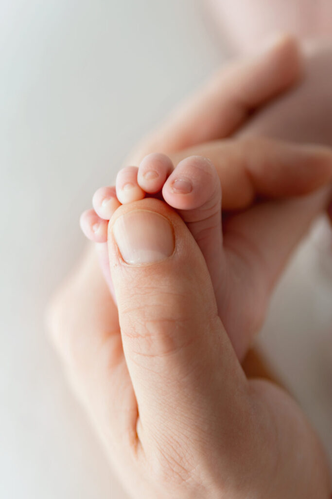 An adult hand gently holding a newborn’s foot