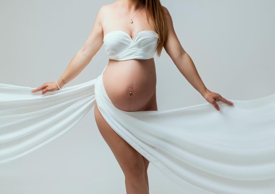 Femme enceinte en robe blanche fluide en studio, portrait maternité artistique et doux
