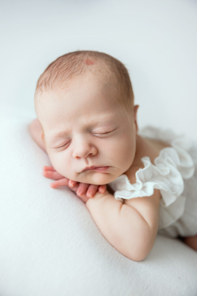 Bébé nouveau-né endormi en gros plan, allongé sur fond blanc, vêtu d'une robe blanche délicate - photo de naissance professionnelle