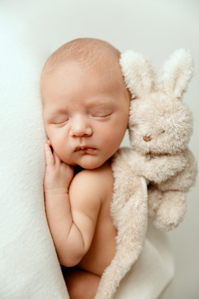Nouveau-né endormi serrant une peluche lapin blanc, photo de naissance professionnelle