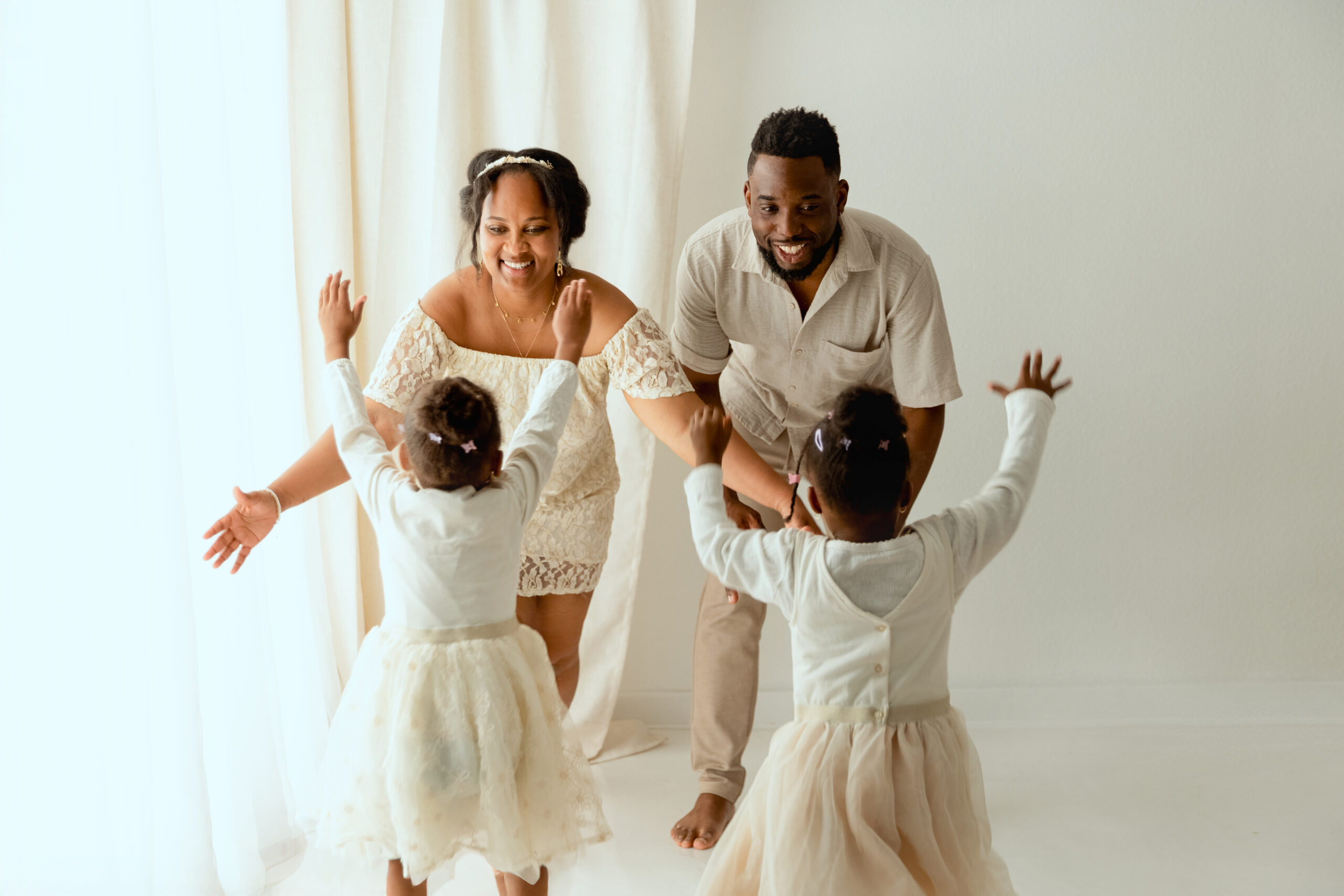Famille heureuse avec deux enfants jouant ensemble en studio photo, vêtus de tenues blanc crème coordonnées