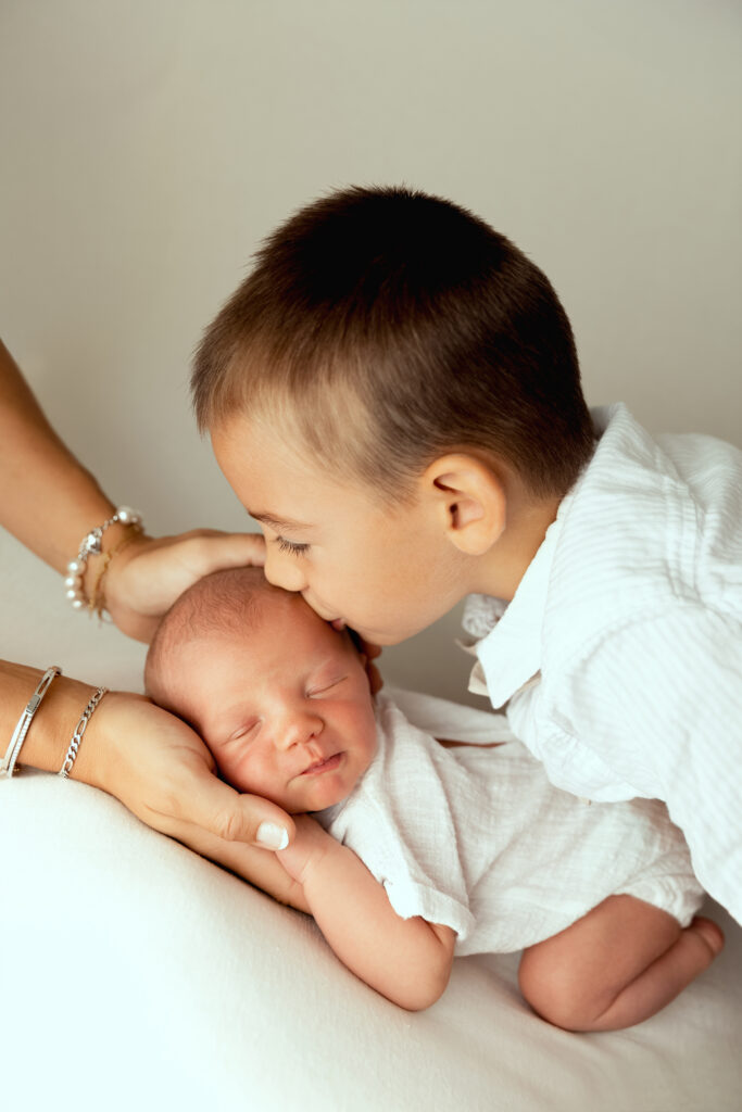 Grand frère embrassant son petit frère nouveau-né lors d'une séance photo famille Mlle L Photographie Annemasse