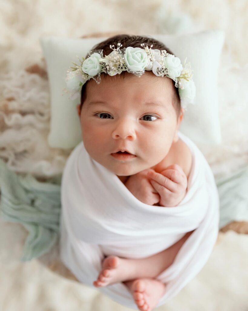 Bébé nouveau-né enveloppé de blanc avec couronne de fleurs blanches en studio photo, photographe bébé à Annemasse, près de Genève