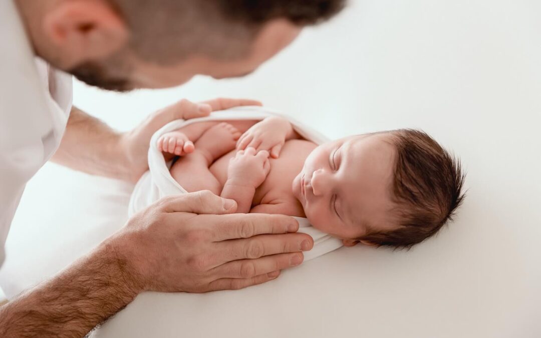 Bébé nouveau-né endormi dans les mains de son père lors d'une séance photo professionnelle, photographe nouveau-né entre Genève et Annecy