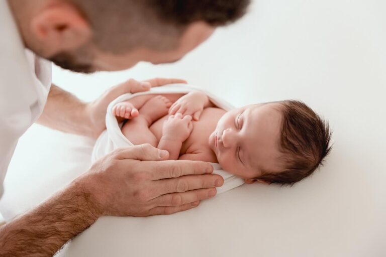 Bébé nouveau-né endormi dans les mains de son père lors d'une séance photo professionnelle, photographe nouveau-né entre Genève et Annecy