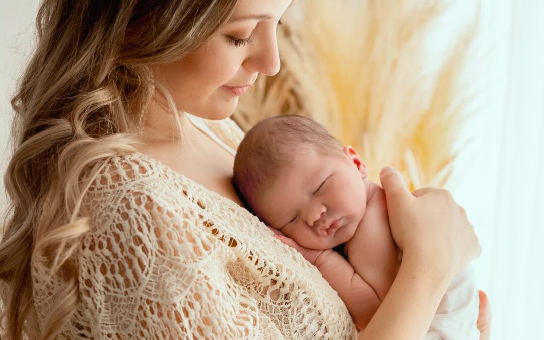 Mère tenant tendrement son nouveau-né endormi dans les bras, photographie douce et lumineuse en studio, photographe nouveau-né entre Genève et Annecy