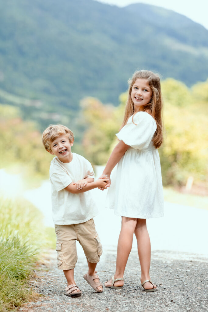Two smiling children holding hands on a path, mountains in the background, family photo in Haute-Savoie
